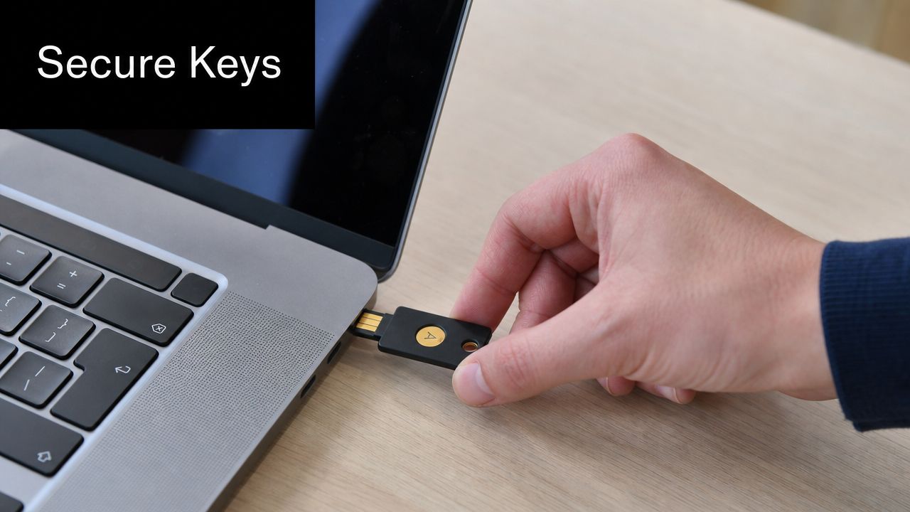 A person inserts a black hardware security key into the USB port of a silver laptop.